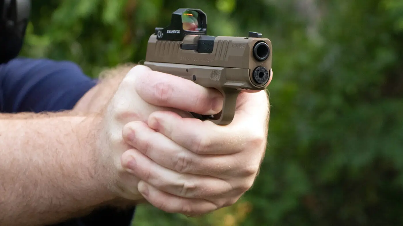 Two-handed grip on a pistol with a red dot sight, aimed at the range