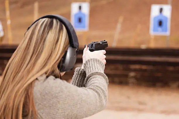 Woman wearing ear and eye protection aiming a handgun at an indoor range